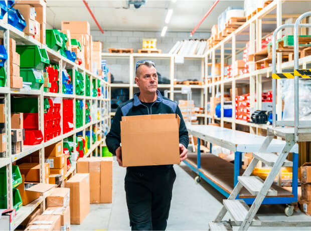 Trabajador En Un Almacén Organizando Cajas, Rodeado De Estantes Llenos De Productos Y Suministros